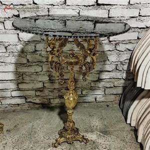 میز برنجی تک پایه مدل چهار فرشته با بدنه ی پر کار و رویه شیشه ای دودی،